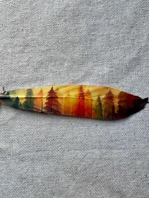 Colorful feather with a forest design on a gray fabric background