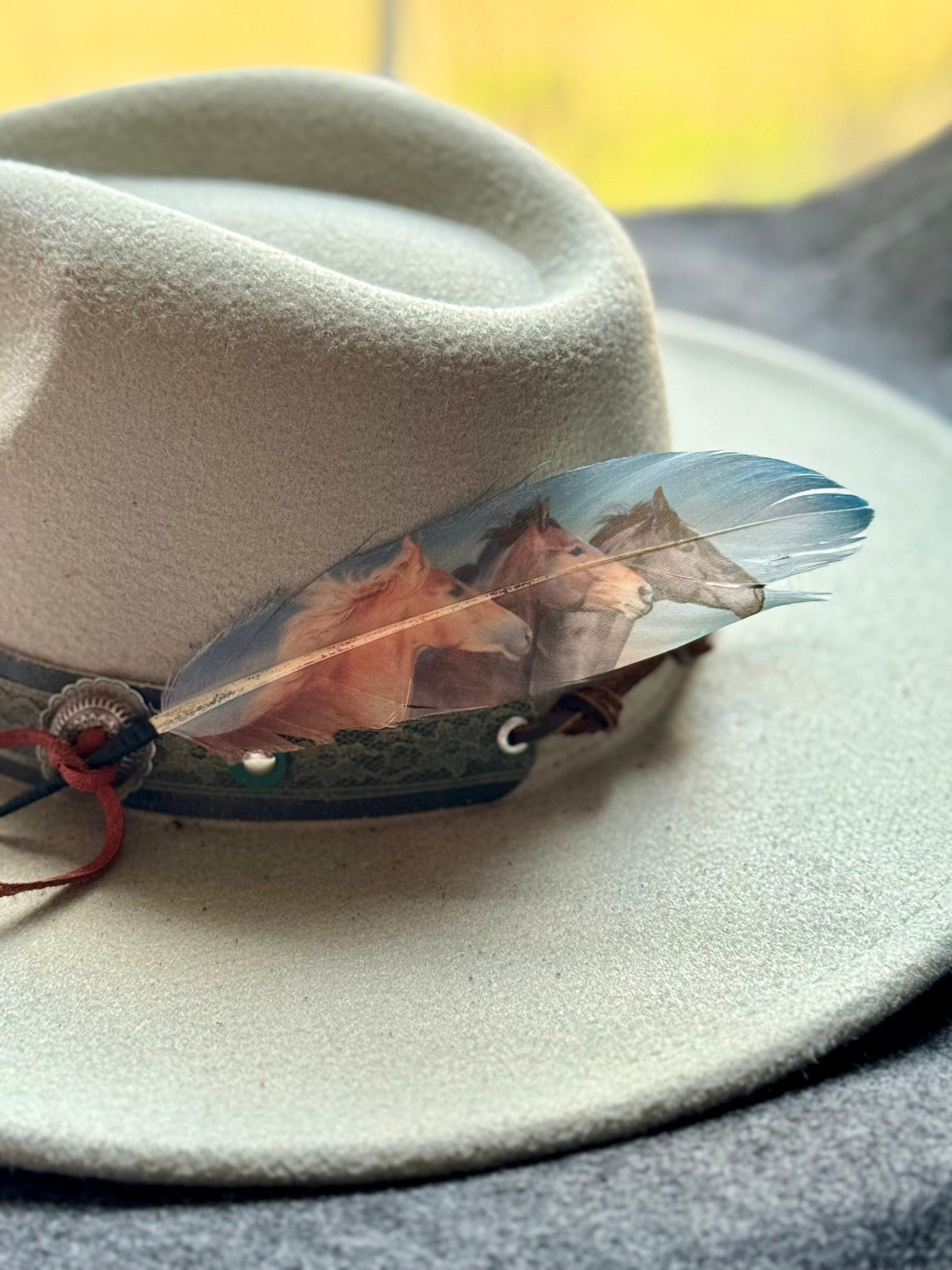 White hat with a decorative feather featuring a horse design on a blurred background