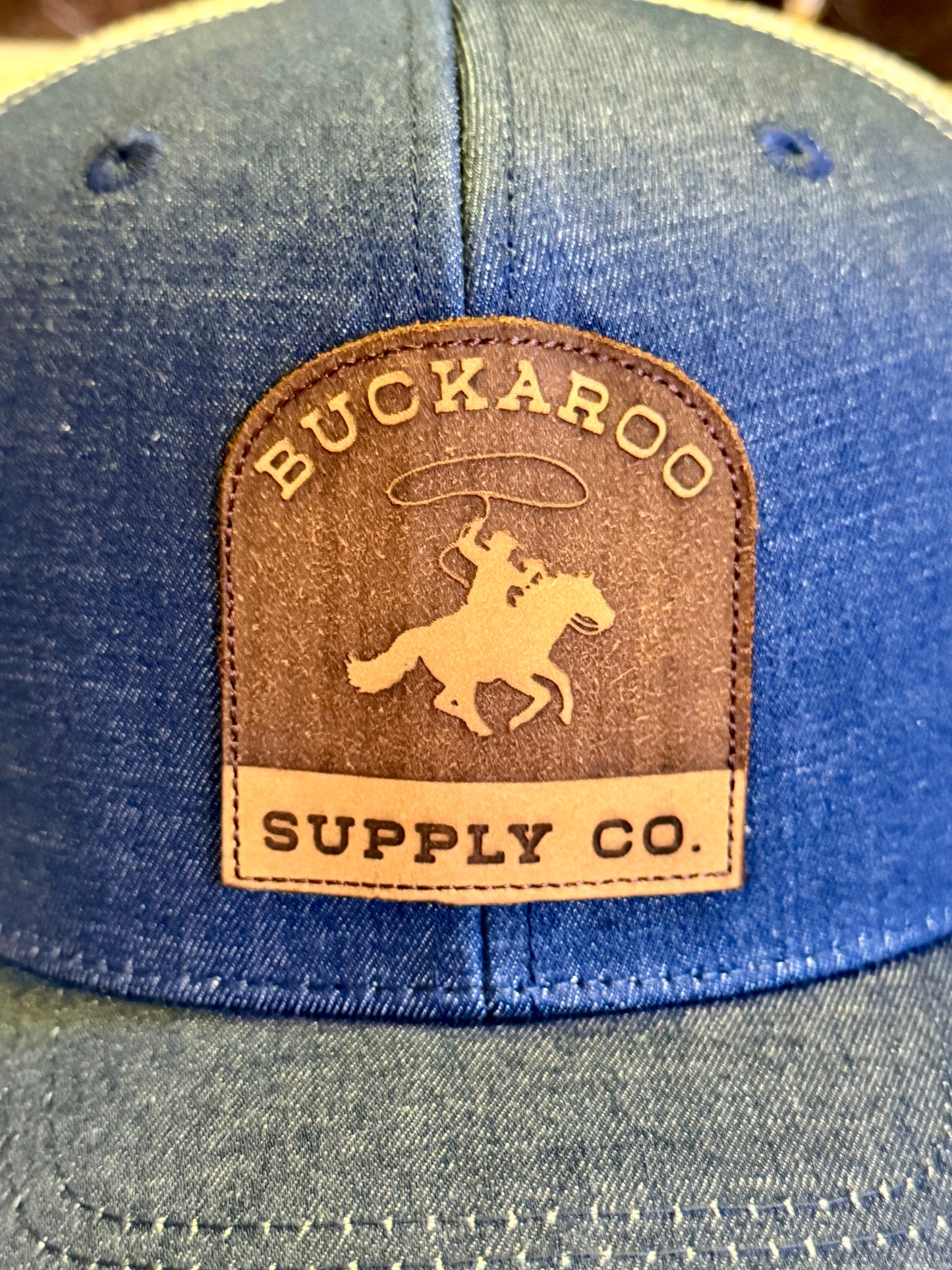 Close-up of dimensional Buckaroo Supply Co. leather patch on denim trucker hat