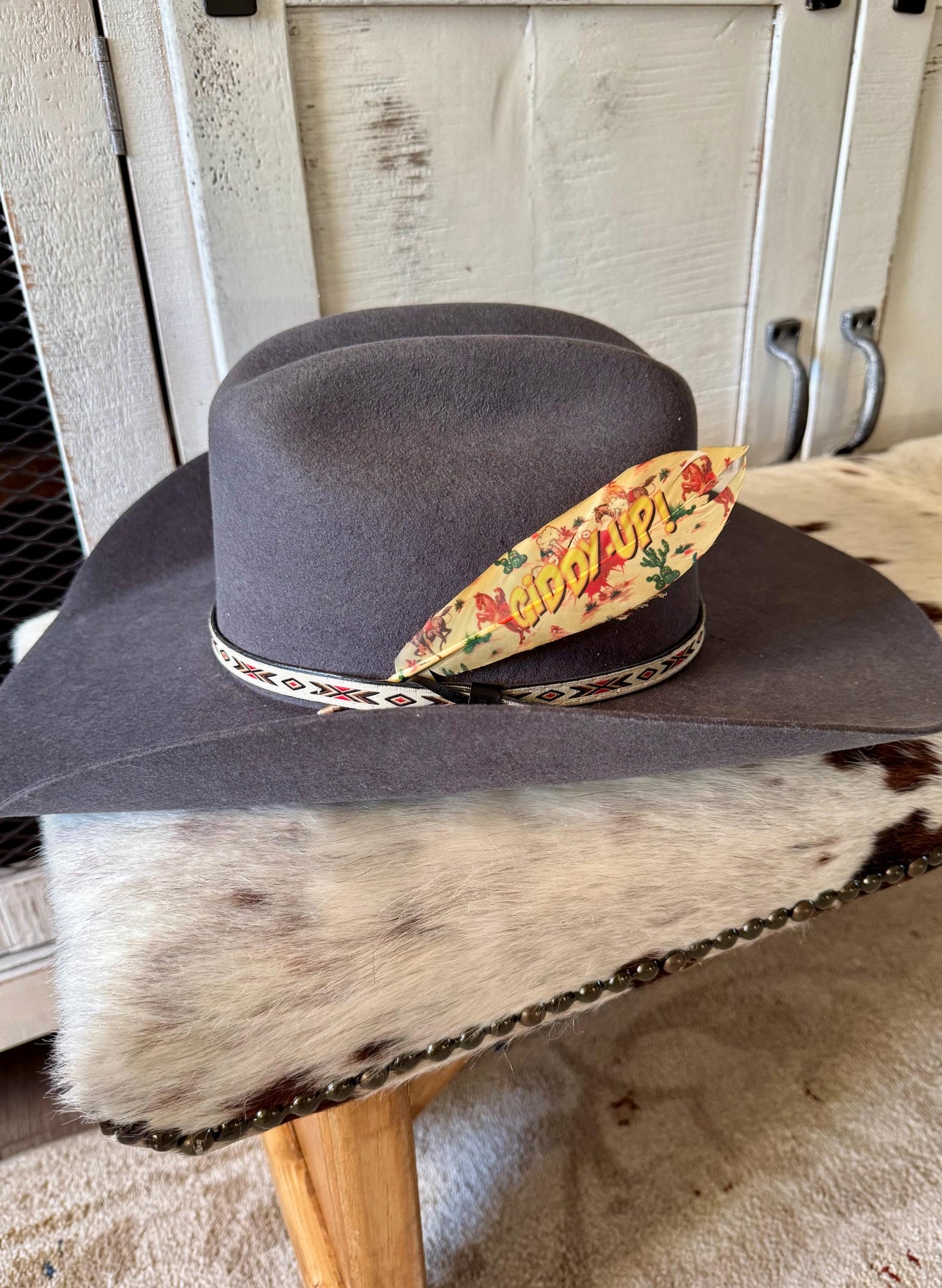 Gray cowboy hat with a colorful feather and decorative band on a wooden surface.