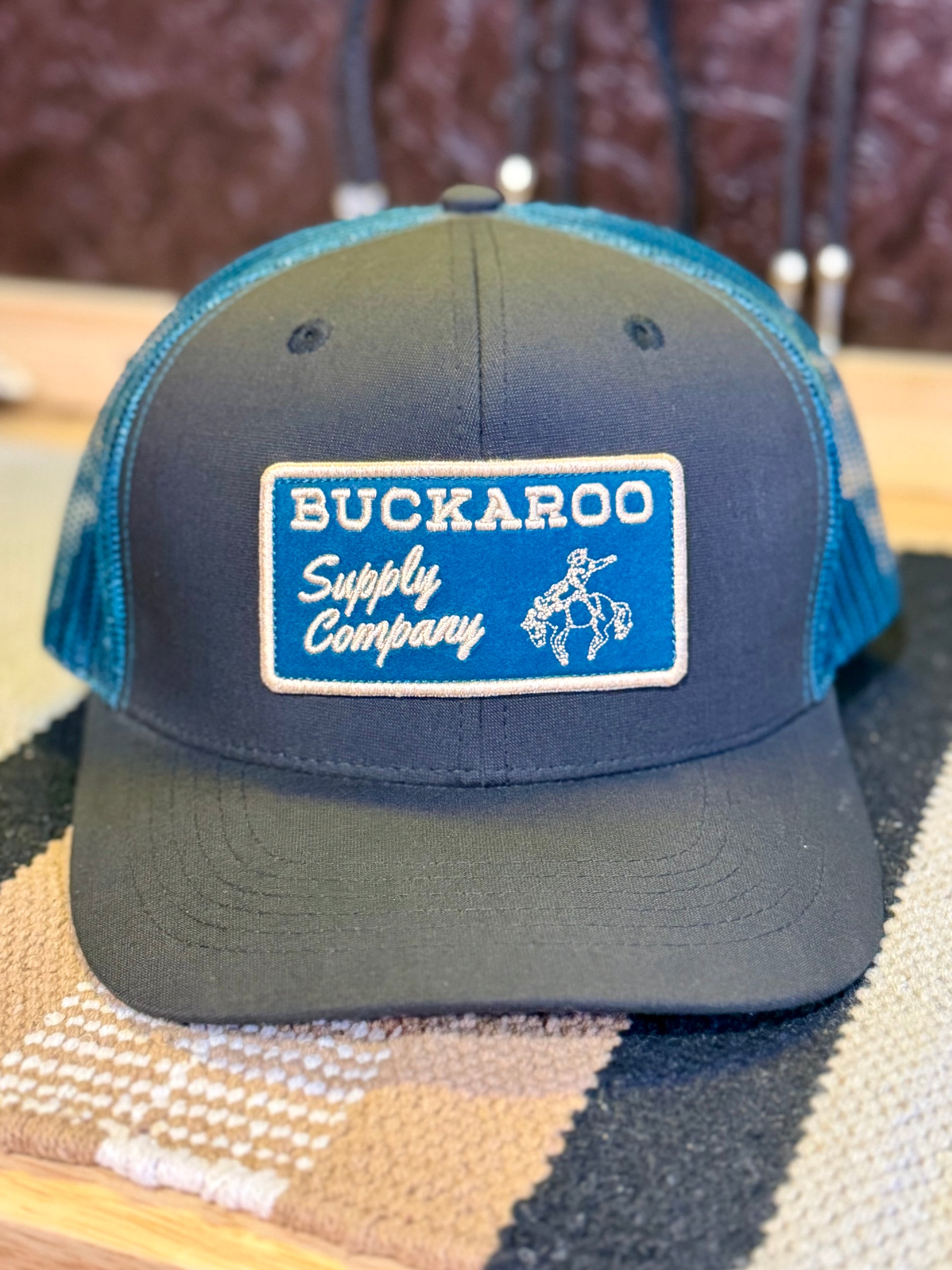 Front view of black and teal Western trucker hat with Buckaroo Supply Company patch
