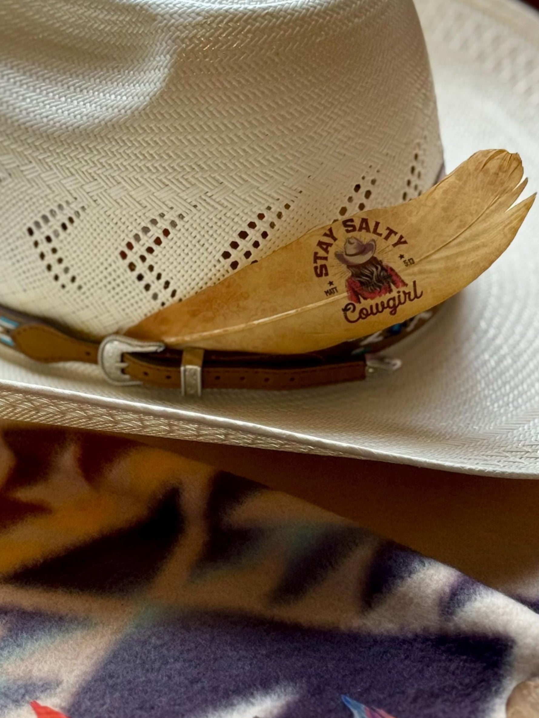 Cowboy hat with decorative band and feather on a colorful fabric background