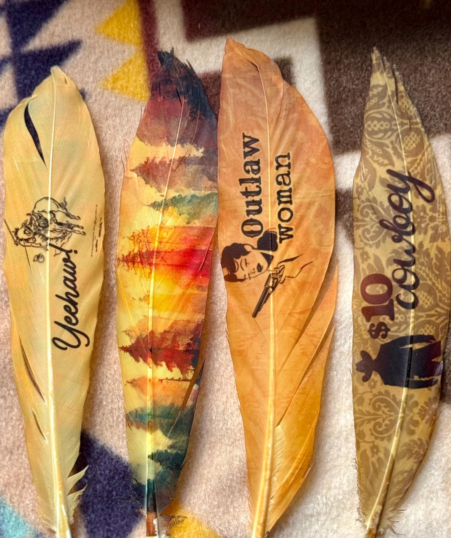 Four decorative feathers with various designs and text on a textured surface.
