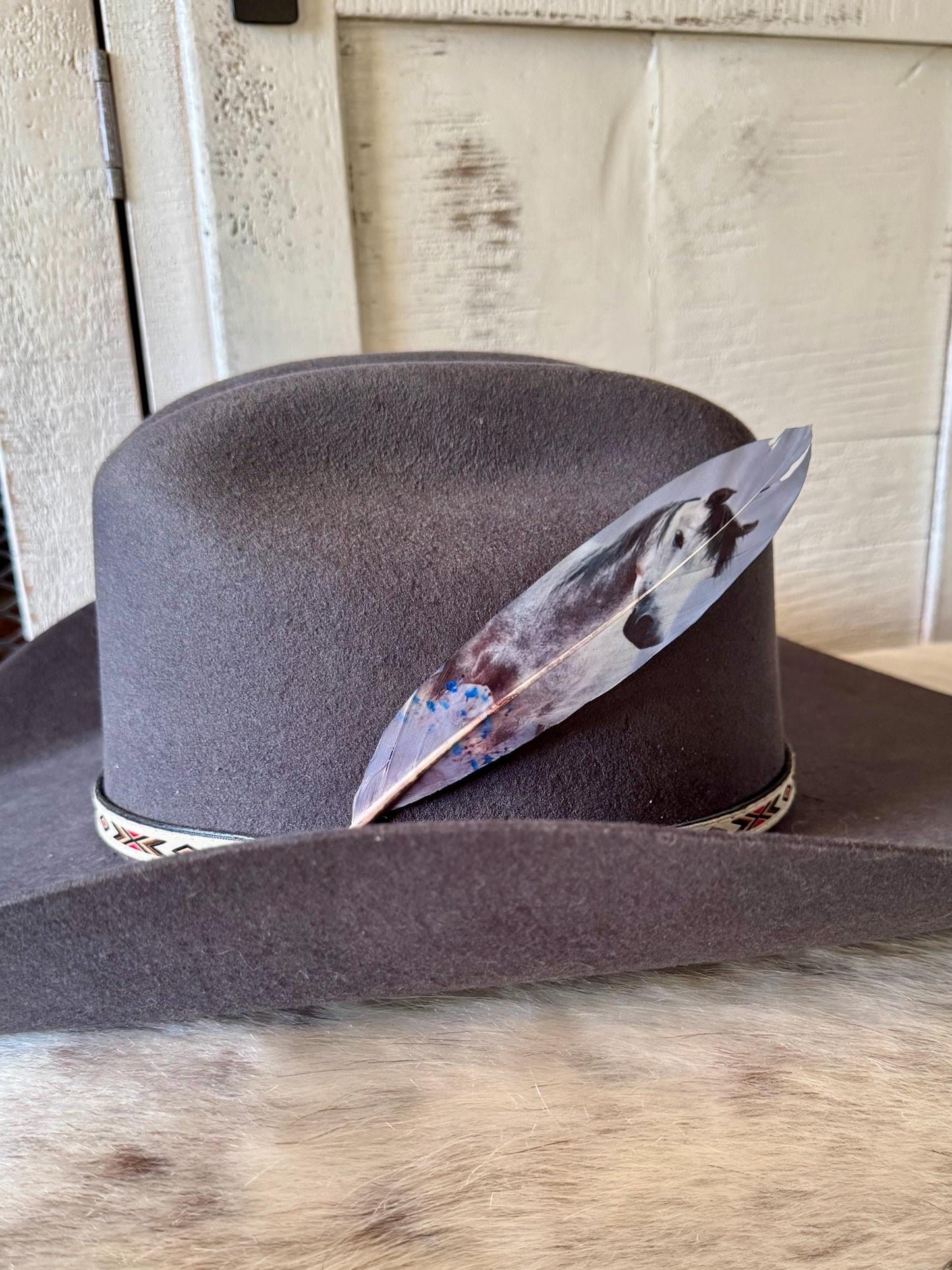Gray cowboy hat with a Buckaroo Supply Co. feather on a wooden surface