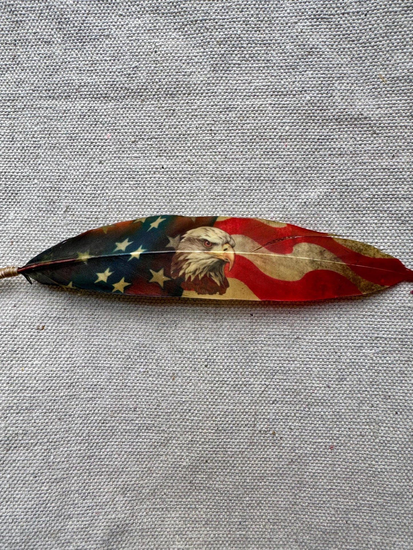 Decorative feather with American flag design on a gray fabric background