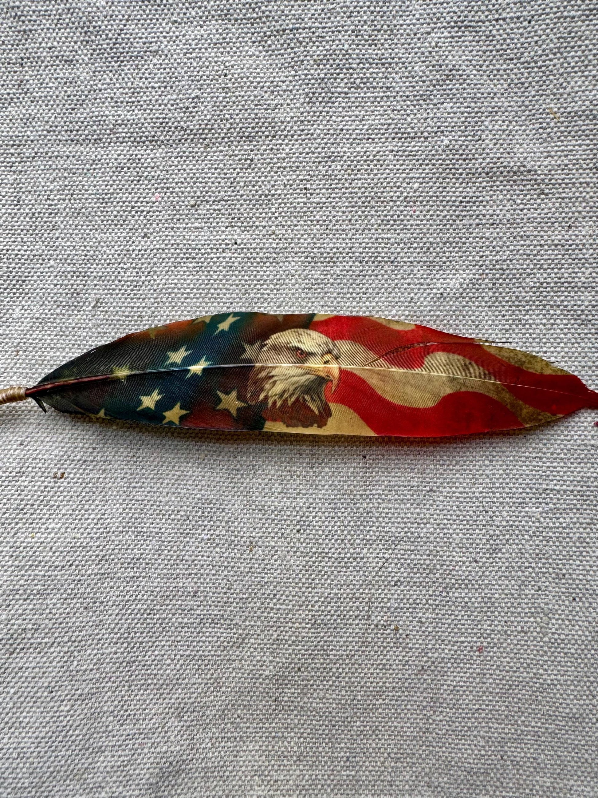 Decorative feather with American flag design on a gray fabric background