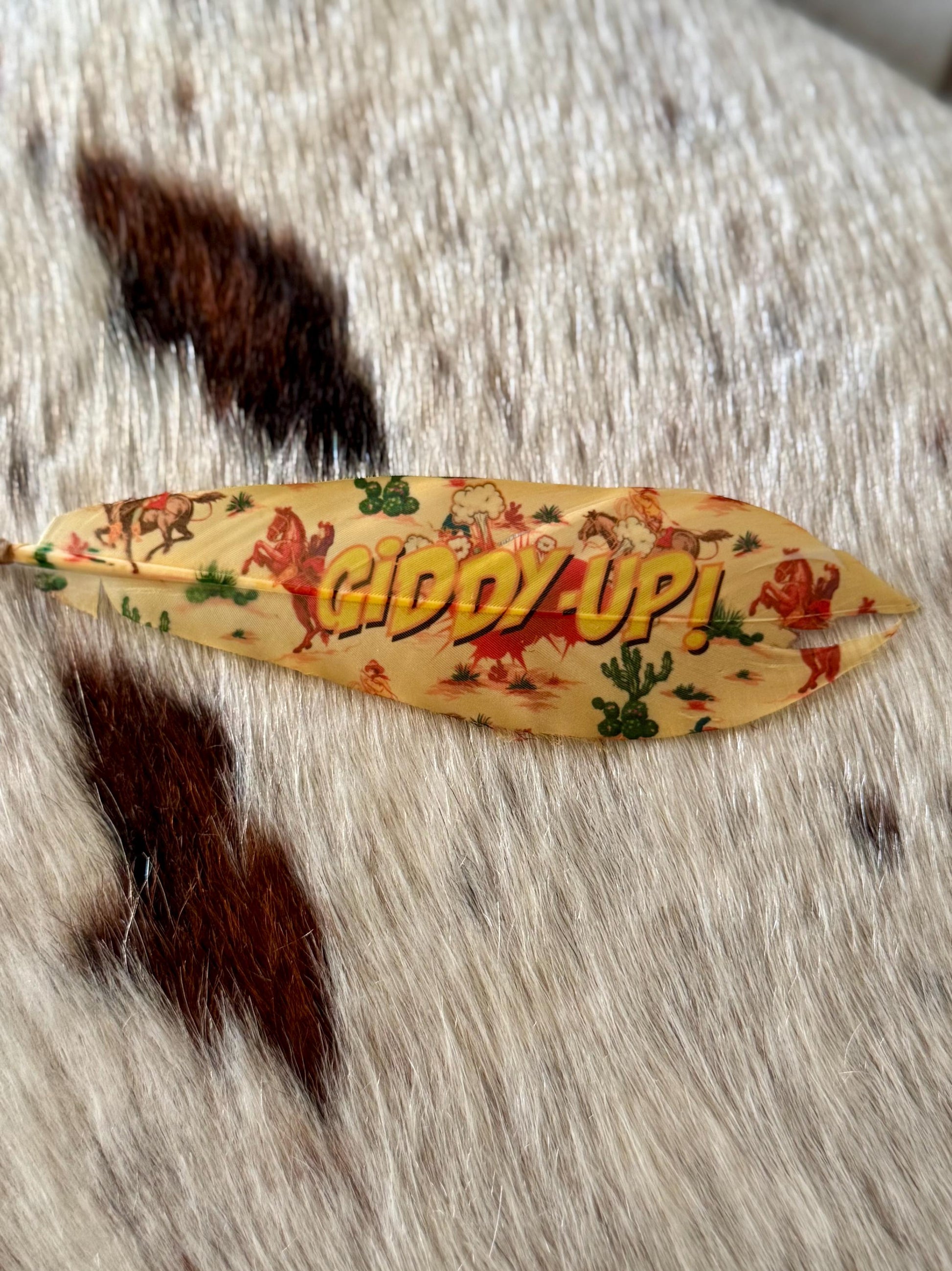 Decorative feather with 'Giddy Up!' text on a fur background