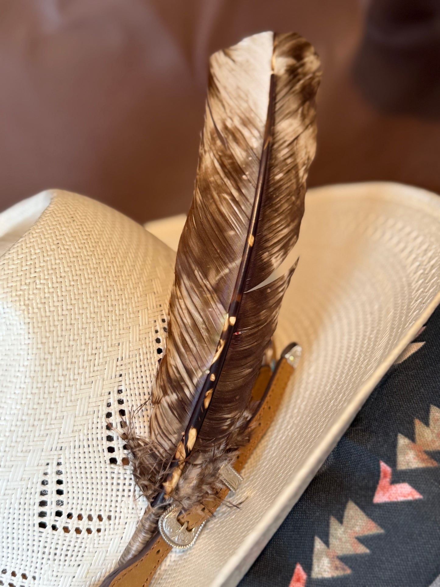 A close-up of a woven straw cowboy hat with a brown feather and a tan leather strap resting on the brim.