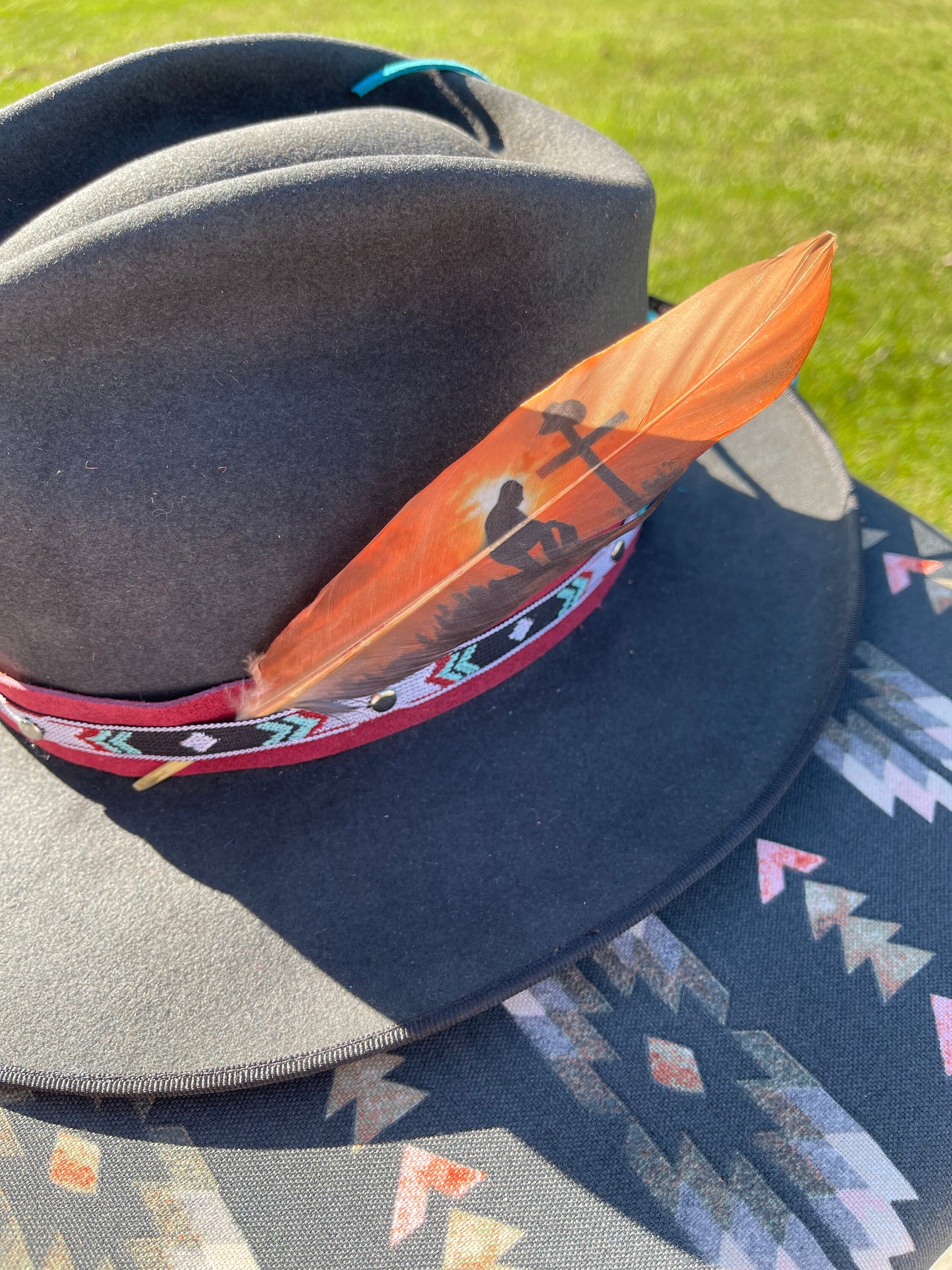 Gray hat with an orange feather and patterned band on a grassy background