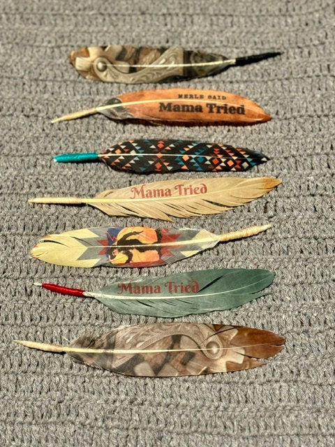 Feathers with 'Mama Tried' text on a textured surface