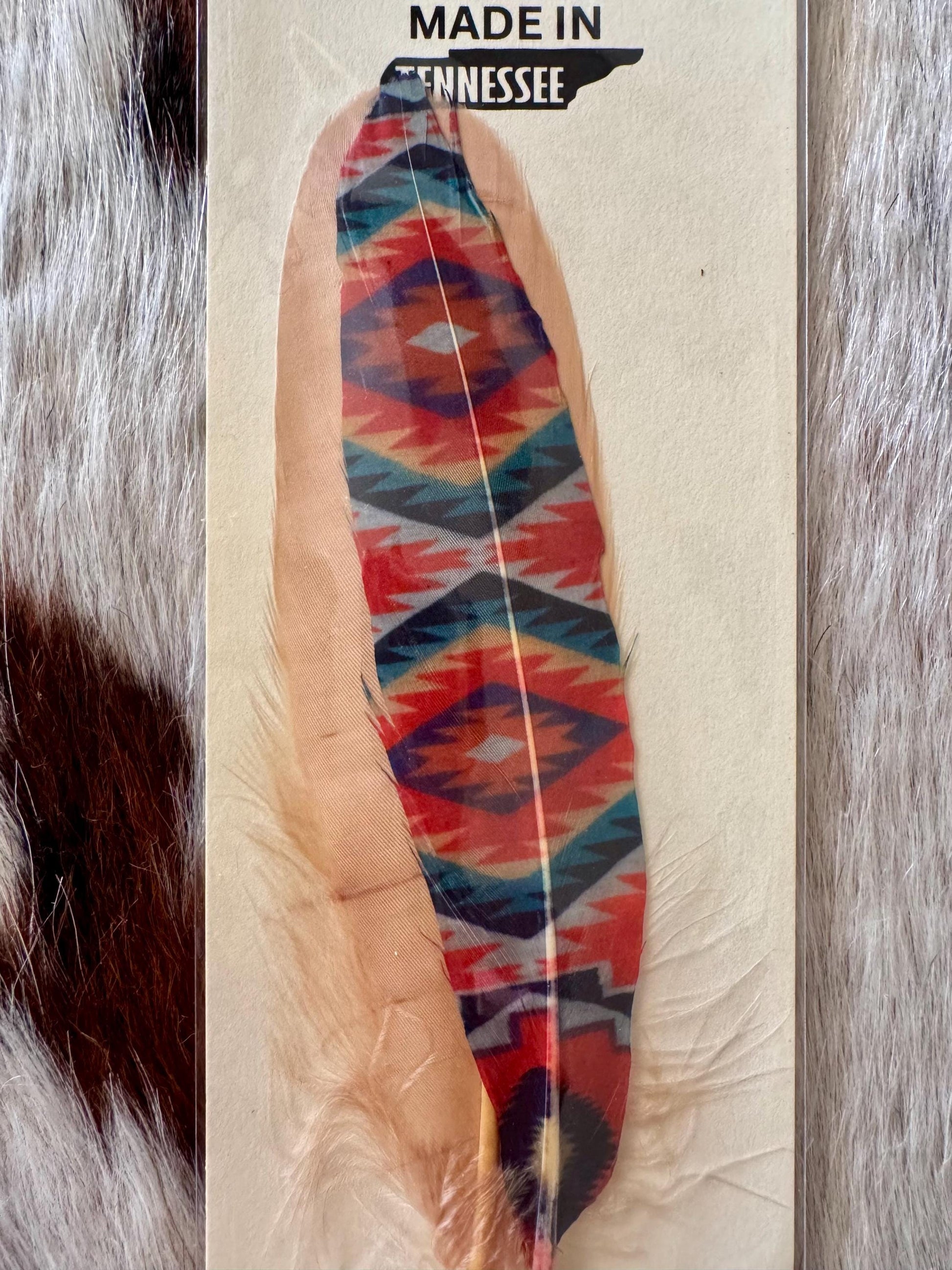 Colorful feather with geometric pattern on a textured background, 'Made in Tennessee' label above.