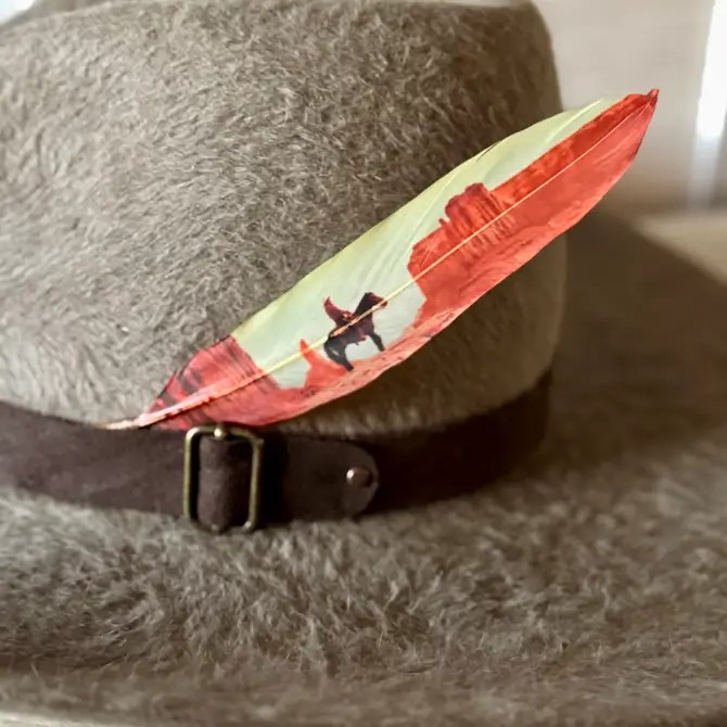 Desert Cowboy Western hat feather with cowboy silhouette and red rock desert scene on a gray felt hat