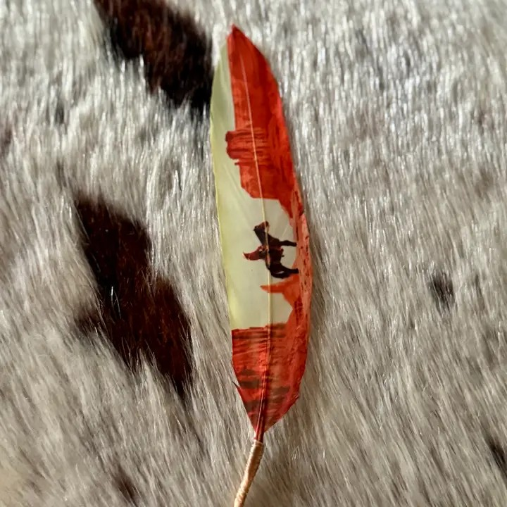 A single decorative feather with red, cream, and black painted details lies on a textured black-and-white fur surface.
