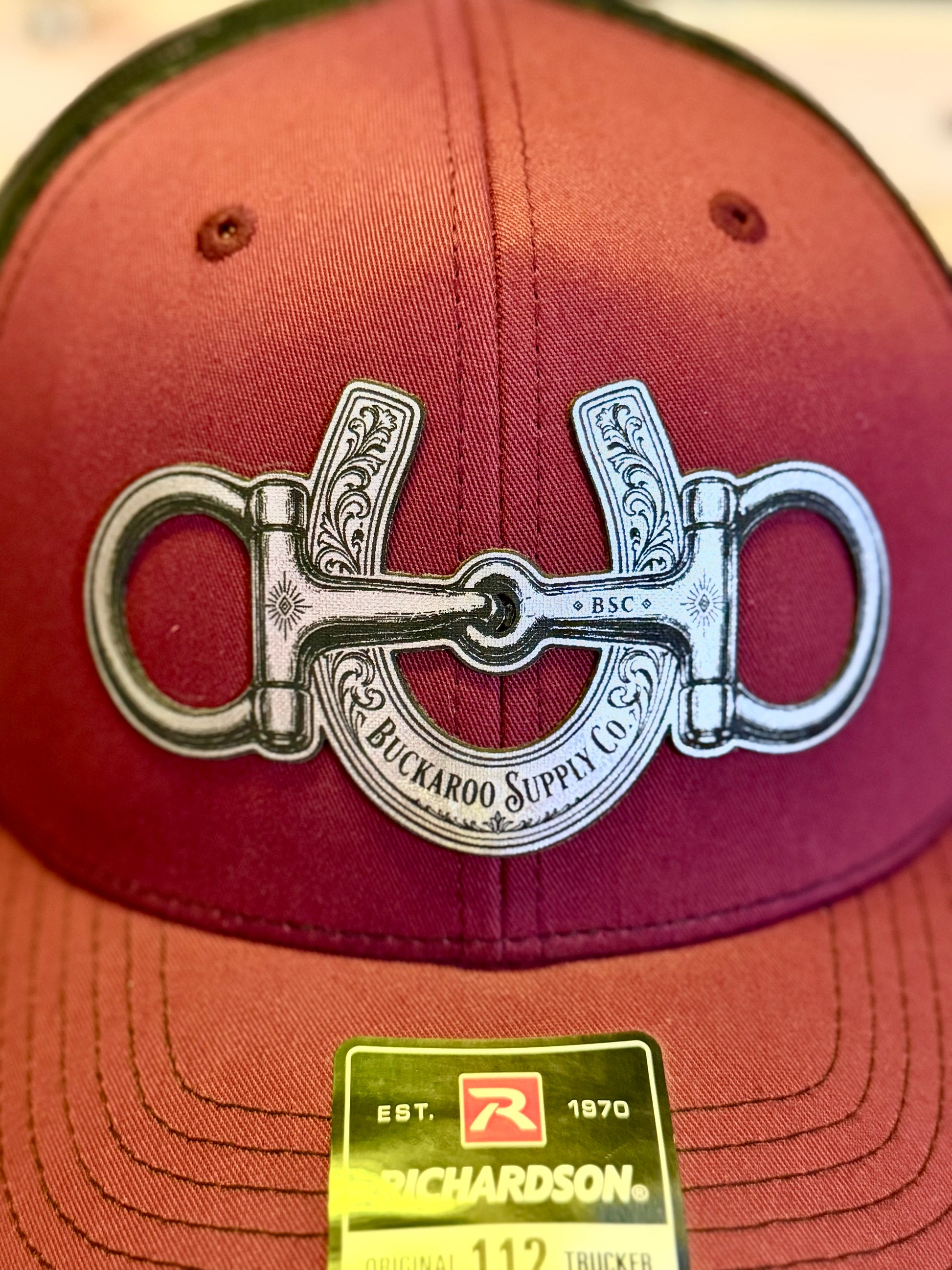 Close-up of silver-tone snaffle bit and horseshoe artwork on Richardson 112 trucker hat