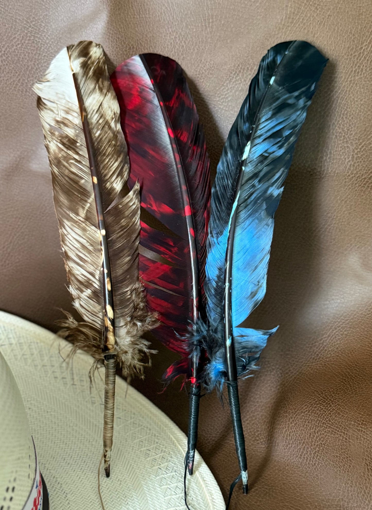 Three decorative feathers with mottled patterns in brown, red, and blue, displayed against a brown textured background.