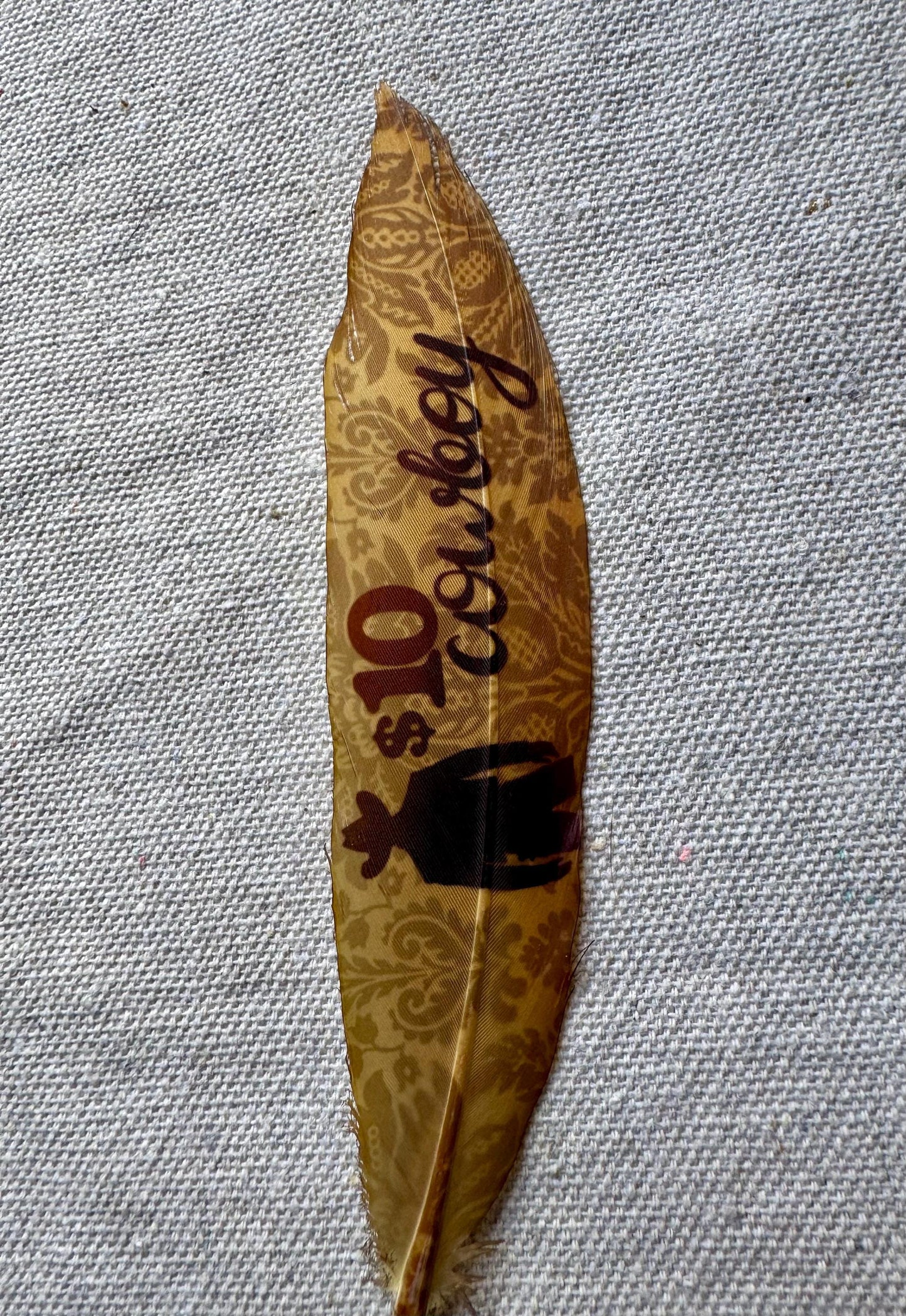 Decorative leaf with 'cowboy' and '$10' printed on it, placed on a textured gray surface.