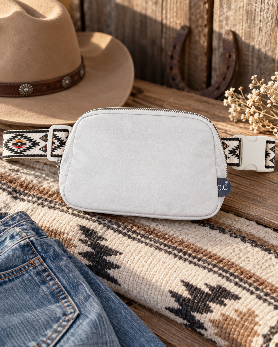 White Southwestern strap belt bag styled with cowboy hat, denim and rustic Western decor