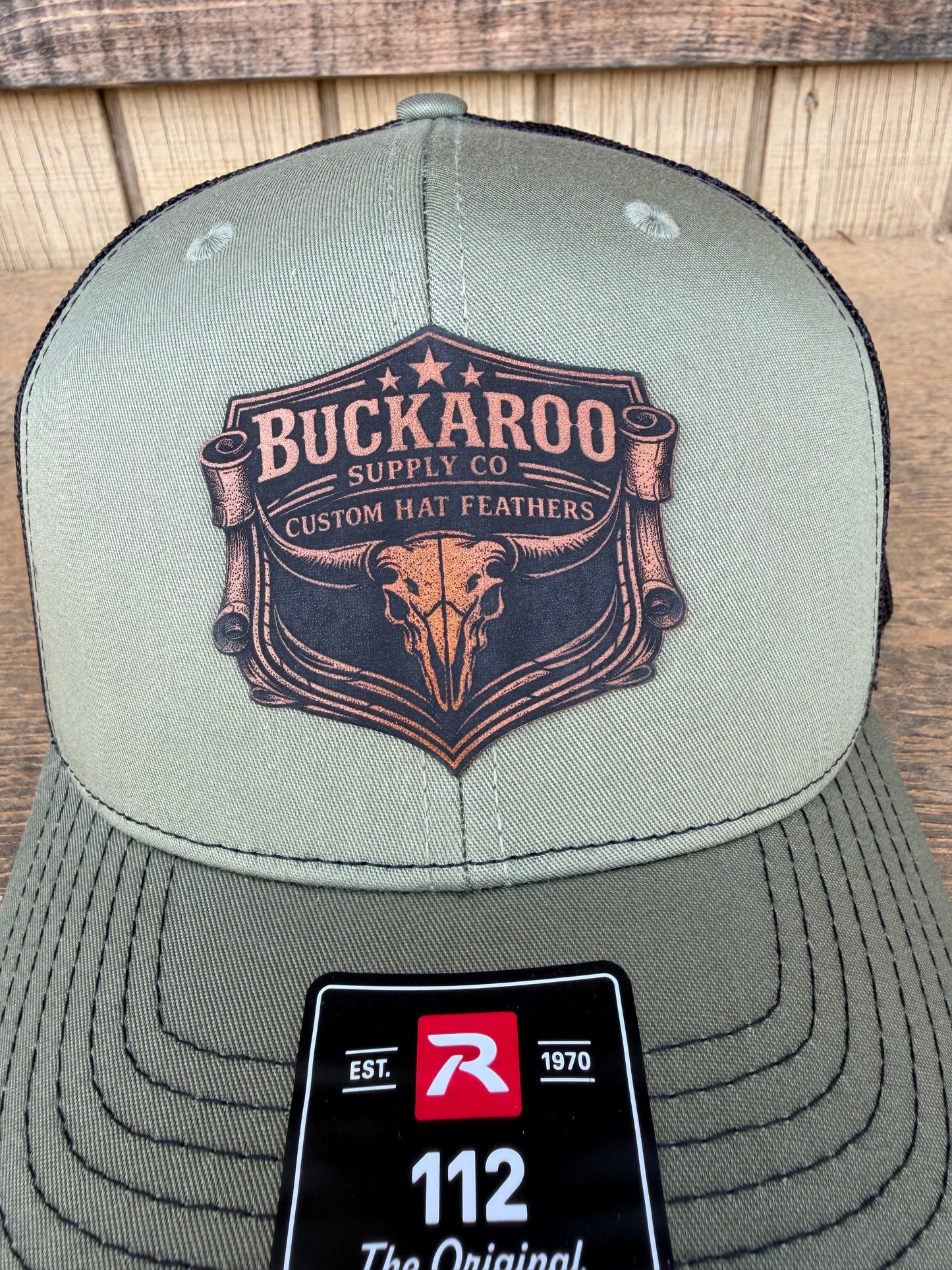 Green cap with 'Buckaroo Supply Co' logo and R leaf brand tag on a wooden surface