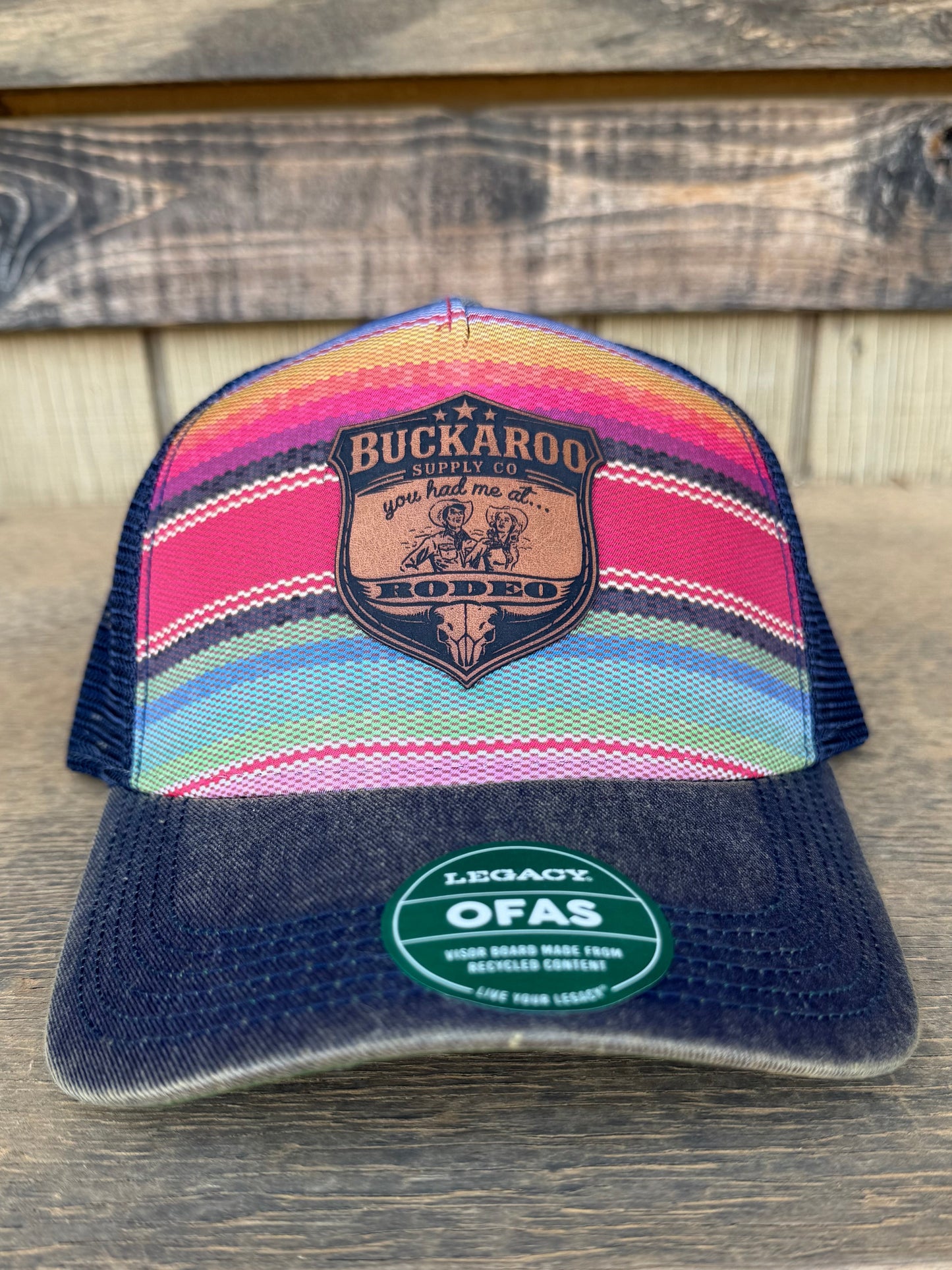 Colorful striped hat with a logo on a wooden surface. Colorful serape striped trucker hat with a Buckaroo Supply Co logo.