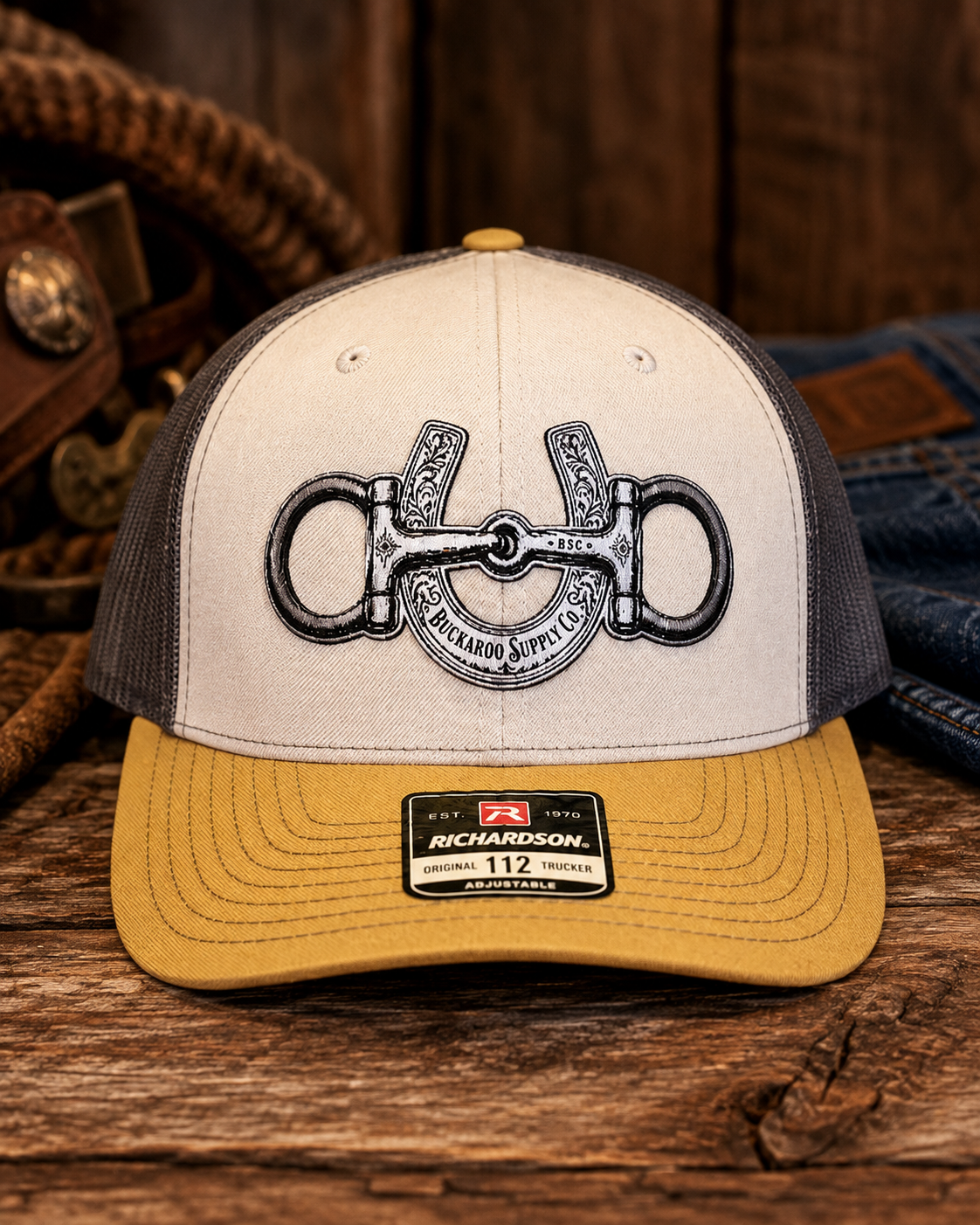 Snaffle Bit and Horseshoe Richardson 112 Western trucker hat in Mink Beige Charcoal and Amber Gold on rustic wood