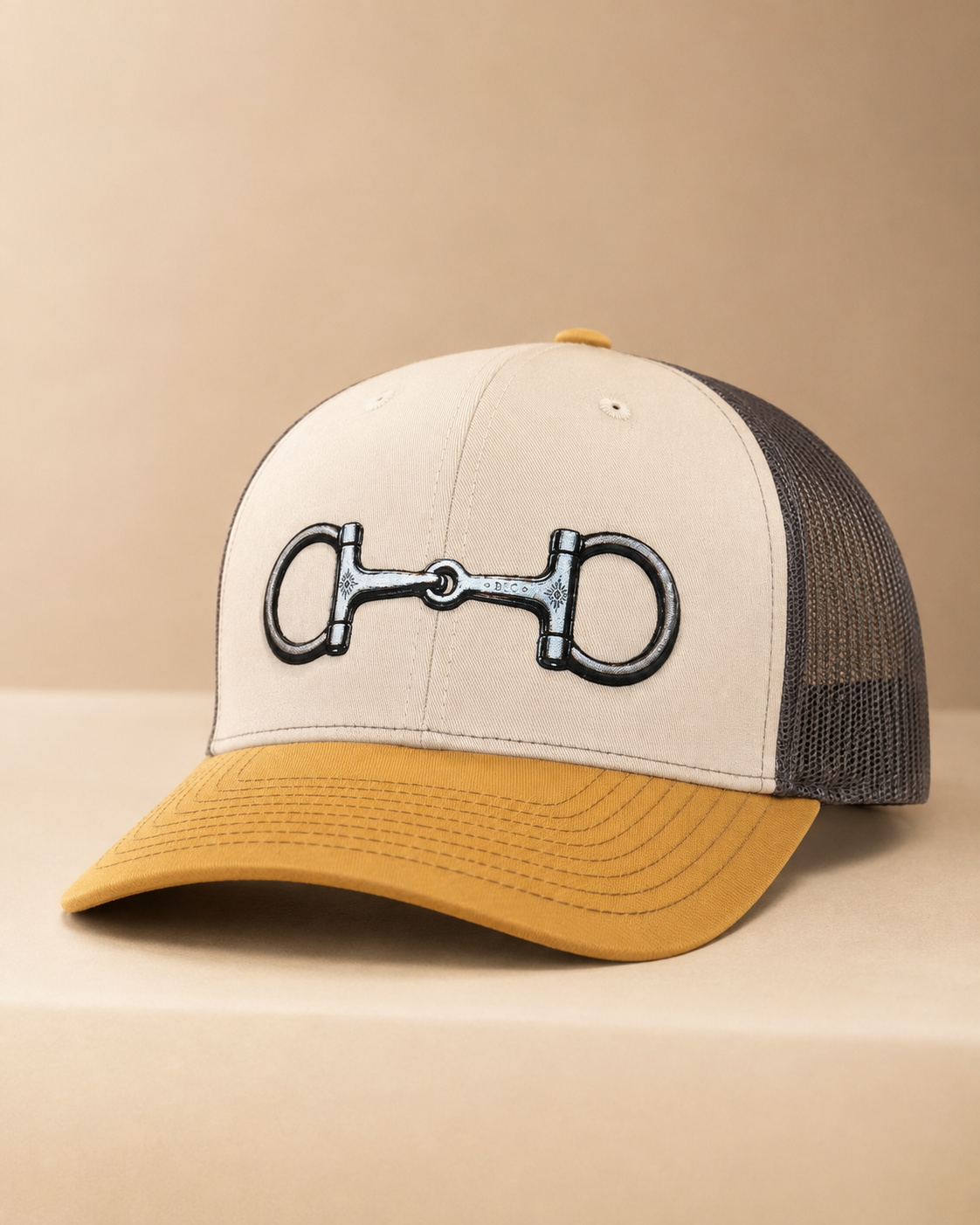 Mink beige, charcoal, and amber gold Richardson 112 trucker hat with Buckaroo Supply Co. snaffle bit design