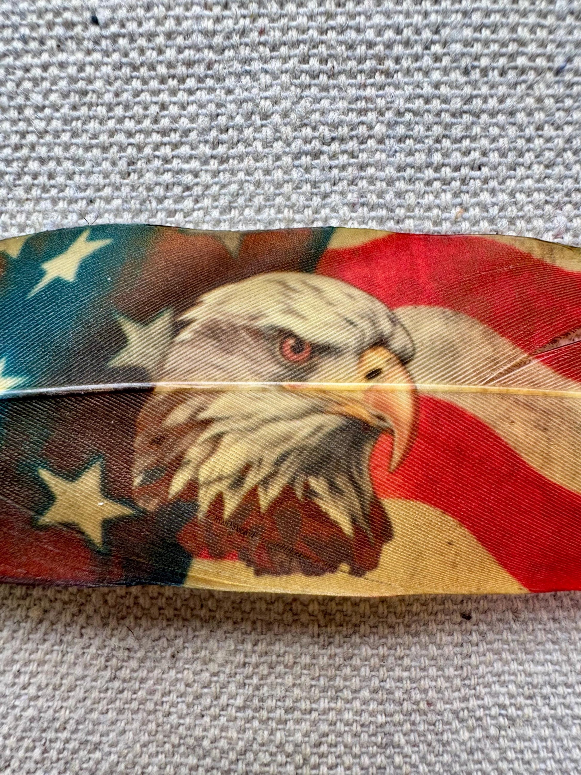 Feather with an eagle and American flag design on a textured fabric background