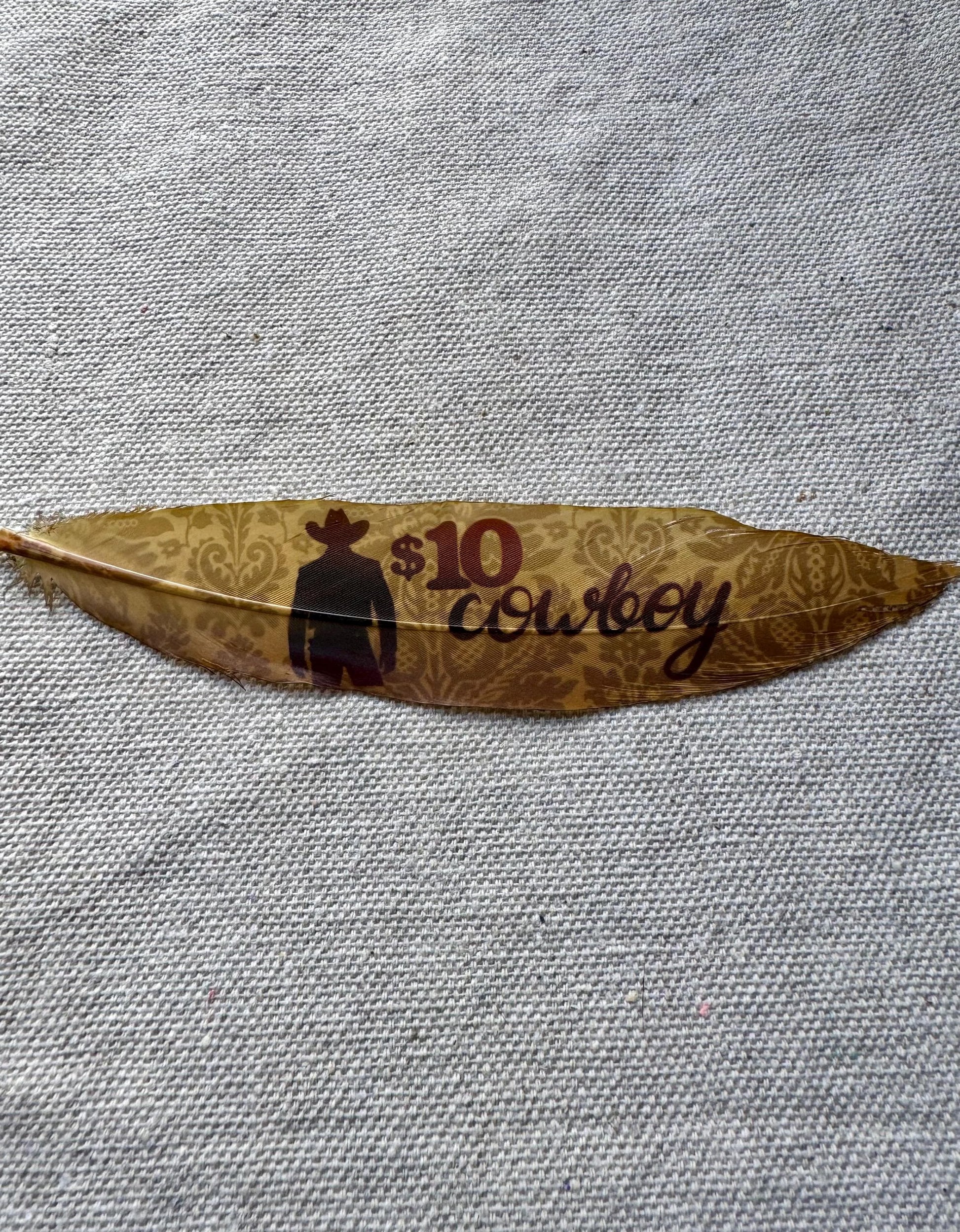 Feather with '10 Cowboy' text and logo on a textured gray background