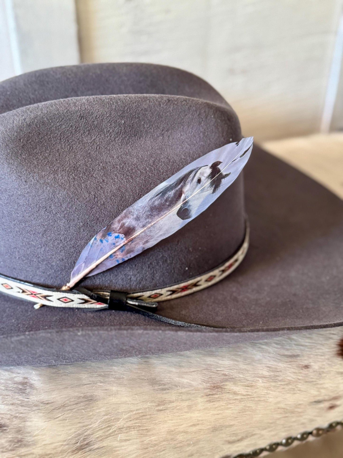 Cowboy hat with a decorative band and Buckaroo Supply Co. feather on a wooden surface