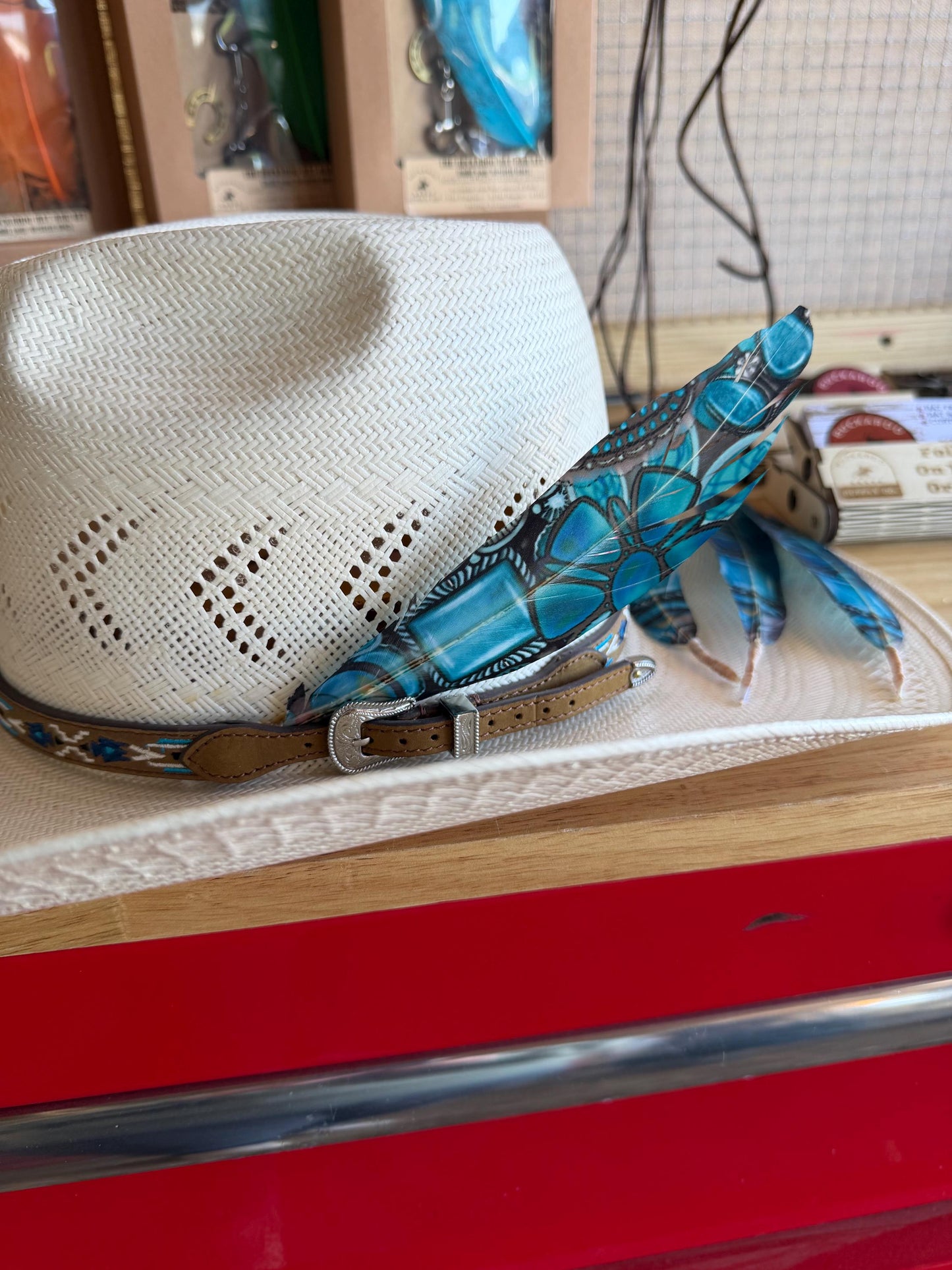 Blue turquoise Western hat feather displayed on a straw cowboy hat