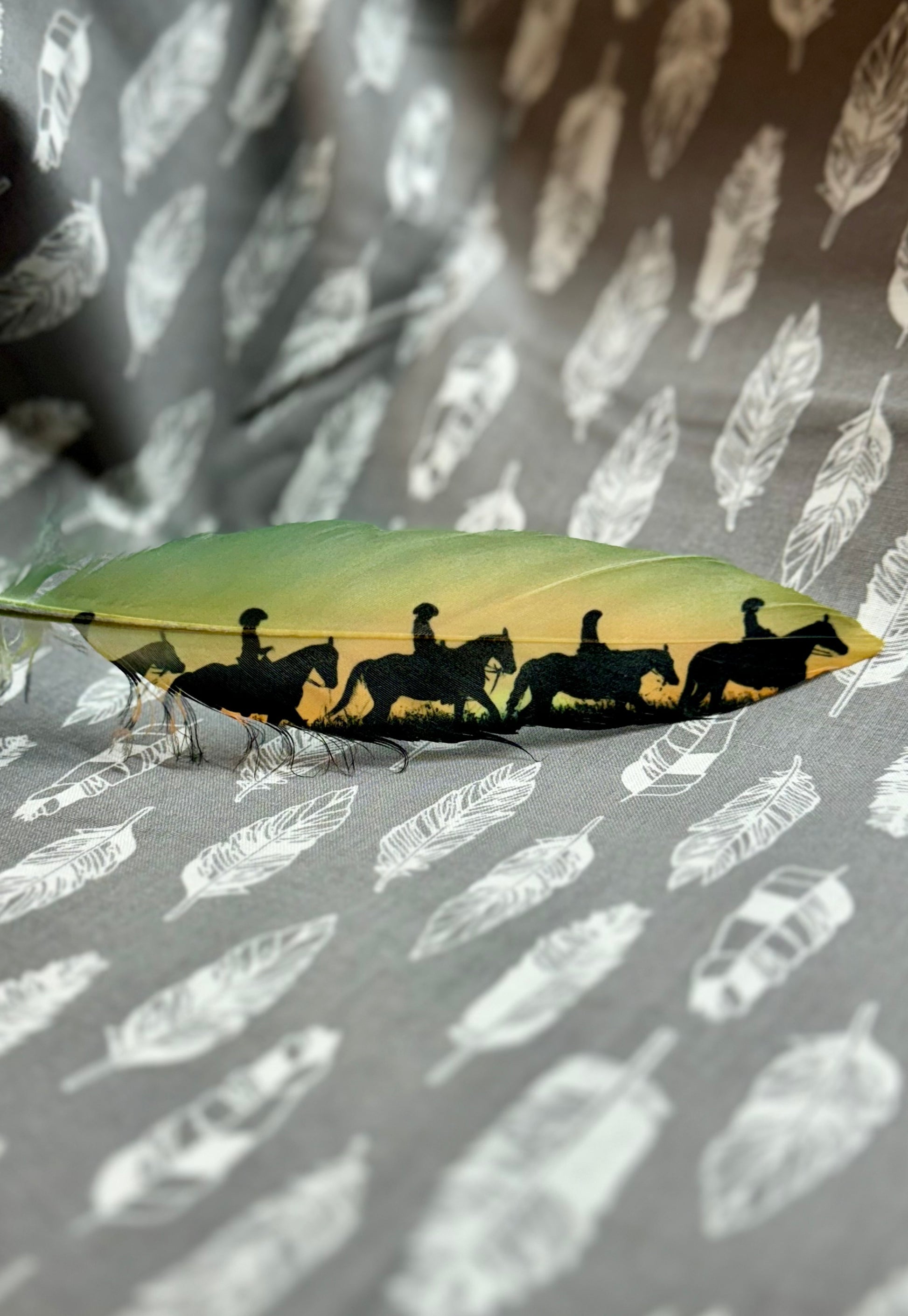 Buckaroo Supply Co. hat feather with black silhouette of people on horses against a feather-patterned background