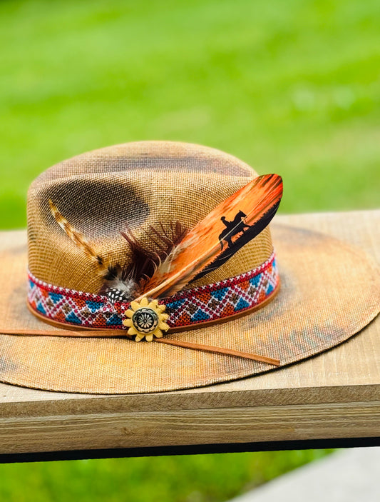 Straw hat with feather and decorative band on a wooden surface with grass background